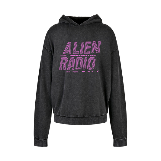 Front: “ALIEN RADIO” printed in pink on the front of a black hoodie with a subtle stone washed finish. The font is large block lettering with two sets of lines sitting within the outline of each letter, and each word is underlined with fragmented lines. The design is centered on the chest.