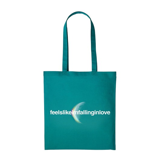 Front: feelslikeimfallinginlove written in white. A crescent moon glows from behind with an eclipsing light dispersion: from the cotton cloud-like white of the moon, to a light greenish hue, to soft pale yellow, to purple, giving it a dreamy, ethereal quality. The fabric is teal, a blueish shade of green.