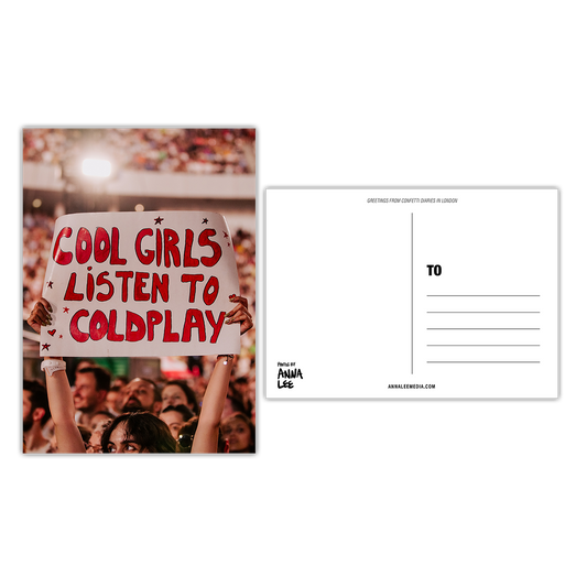 Side-by-side view of a postcard’s front and back. The front features a portrait photo of a fan at a concert holding a large white poster that reads “COOL GIRLS LISTEN TO COLDPLAY” in bold red bubble font. The crowd surrounds her. The back, in landscape orientation, includes a writing space on the left, address lines on the right, “GREETINGS FROM CONFETTI DIARIES IN LONDON” in sloped text at the top, “Photos by Anna Lee” in the bottom right, and “Annaleemedia.com” centered below.