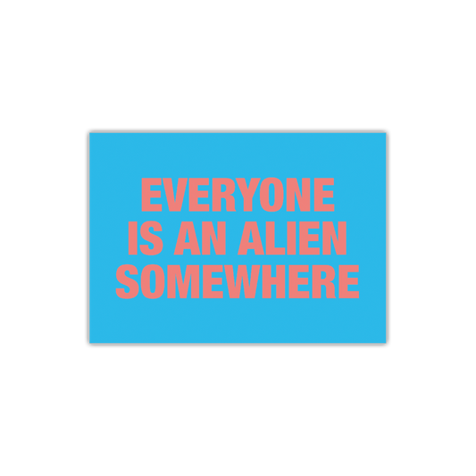 Front: EVERYONE IS AN ALIEN SOMEWHERE in large bold salmon-pink font on the front of a bright blue postcard. The artwork is stacked on three lines. EVERYONE is on the top line, IS AN ALIEN in the middle, and SOMEWHERE is below.