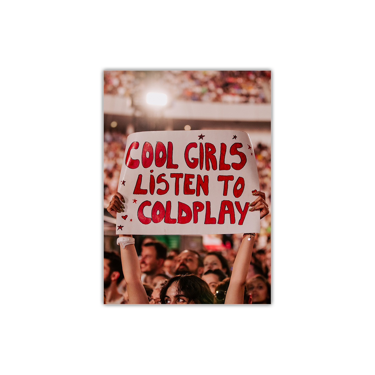 The front features a portrait photo of a fan at a concert holding a large white poster that reads “COOL GIRLS LISTEN TO COLDPLAY” in bold red bubble font. The crowd surrounds her. 